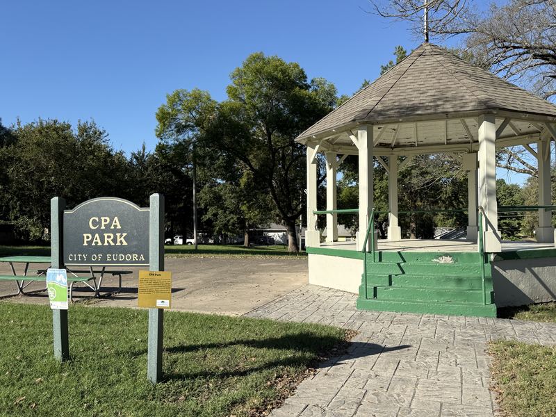 The CPA Park sign next to a white gazebo with green steps, under big shade trees