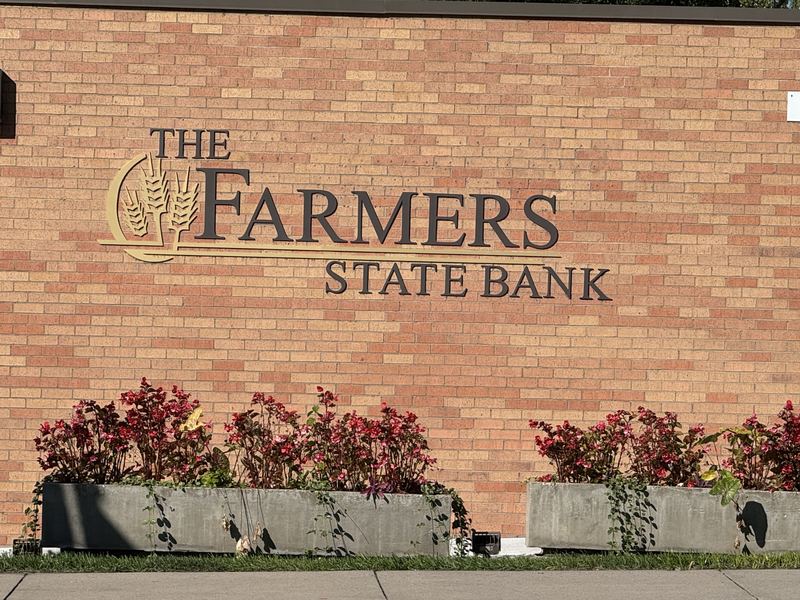 The Farmers State Bank name in gold letters on a red brick wall, above planters full of red flowers